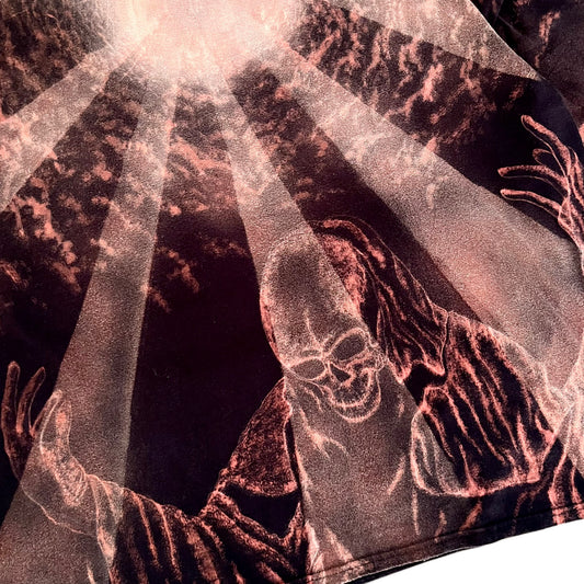 A close-up of a graphic print featuring a grim reaper with outstretched skeletal hands and a skull, rendered in metallic rose-gold and copper tones against a dark background with dramatic light rays.