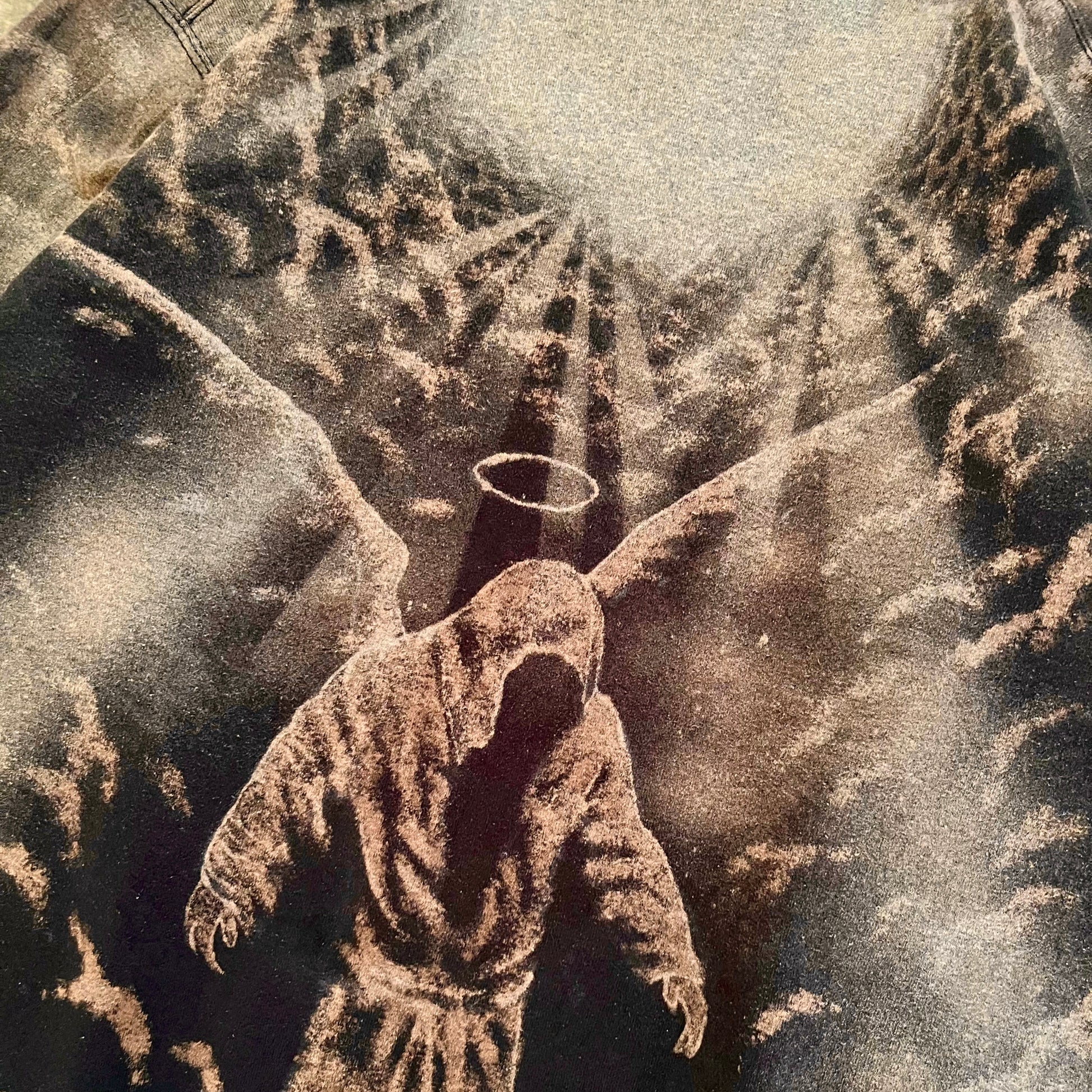 A sepia-toned artwork showing a hooded robed figure with a halo, set against a dramatic cloudy sky with rays of light.