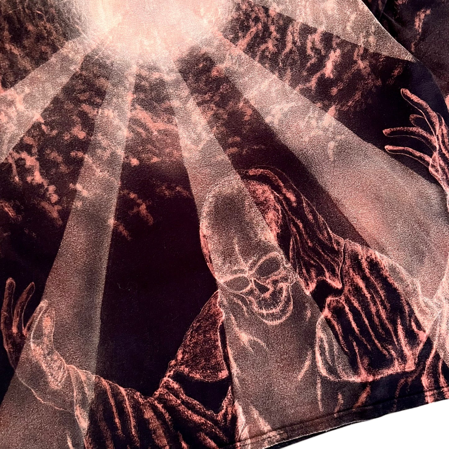 A close-up of a graphic print featuring a grim reaper with outstretched skeletal hands and a skull, rendered in metallic rose-gold and copper tones against a dark background with dramatic light rays.