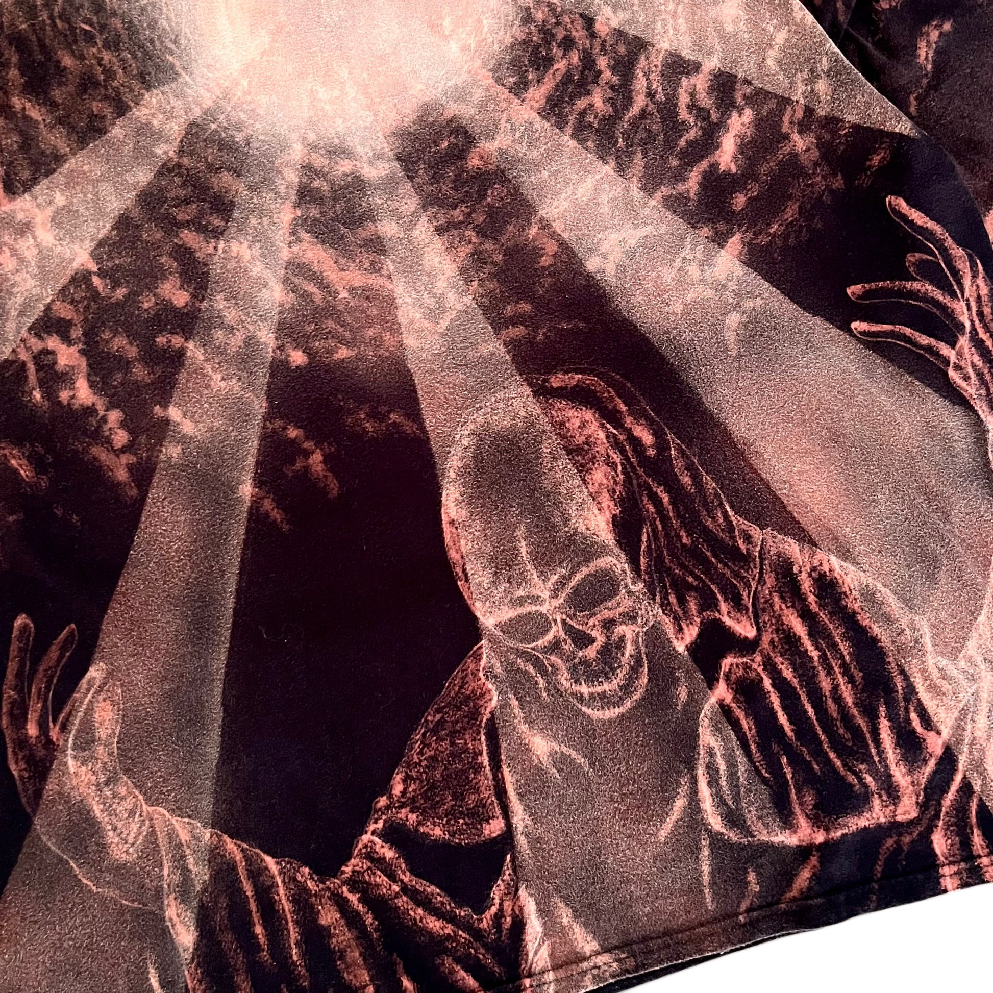 A close-up of a graphic print featuring a grim reaper with outstretched skeletal hands and a skull, rendered in metallic rose-gold and copper tones against a dark background with dramatic light rays.